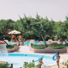 Piscina con bambini che giocano e un fungo d'acqua, circondata da alberi e sdraio.