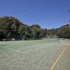 Campo da tennis all'aperto con giocatori in azione circondato da alberi.