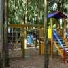 Parco giochi boschivo con scivolo in legno e scalette colorate.