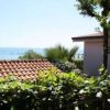 Tetto in tegole rosse, vegetazione e mare sullo sfondo.