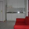Un soggiorno con un divano rosso, cucina a vista e TV su un mobile bianco.