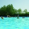 Una piscina affollata con persone che nuotano e alberi sullo sfondo.