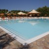 Una piscina all'aperto circondata da lettini e ombrelloni sotto un cielo blu.