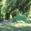 Una tenda verde montata sotto gli alberi, circondata da vegetazione.