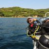 Due subacquei con attrezzatura pronti a immergersi da una barca, con una costa verde sullo sfondo.