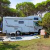 Camper bianco parcheggiato su erba con sedie all'esterno.