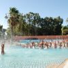 Piscina affollata di persone che si divertono, con spruzzi d'acqua e alberi sullo sfondo.
