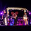 Tre persone su un palco decorato con luci e un clown, durante uno spettacolo notturno.