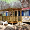 Una casa mobile con un portico in legno tra gli alberi, accessoriata con sedie a sdraio.