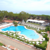 Piscina all'aperto circondata da lettini e ombrelloni, con vista mare e alberi sullo sfondo.