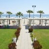 Vialetto con giardino che conduce a una spiaggia con ombrelloni e sedie di fronte al mare.