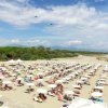 Spiaggia affollata con file di ombrelloni bianchi e persone che godono del mare e del sole.