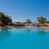 Piscina ampia circondata da palme e ombrelloni, sotto un cielo sereno.