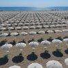 Spiaggia con molti ombrelloni bianchi su sabbia.