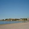 Spiaggia sabbiosa con mare calmo e città sullo sfondo.