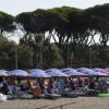 Spiaggia affollata con lettini sotto ombrelloni blu e alberi sullo sfondo.