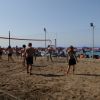 Partita di beach volley sulla sabbia vicino al mare, con ombrelloni sullo sfondo.