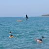 Bagnanti nel mare, kayak arancione e vela nera sullo sfondo.