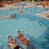 Una piscina con persone che si rilassano, sedie a sdraio e ombrelloni in fondo.