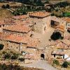 Veduta aerea di un borgo medievale con edifici in pietra e tetti rossicci.