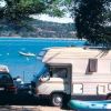 Un camper parcheggiato accanto a un lago con un gommone colorato e un'auto.