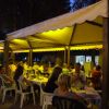 Persone sedute a tavoli sotto una tenda illuminata di notte in un ambiente all'aperto.