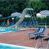 Piscina con sdrai, ombrelloni a righe e uno scivolo. Un bagnante prende il sole.