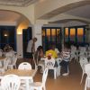 Sala con tavoli e sedie bianche, vista mare al tramonto.