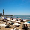 Spiaggia affollata con ombrelloni e faro.