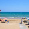 Spiaggia con passerella e torrette, ombrelloni blu e gialli.